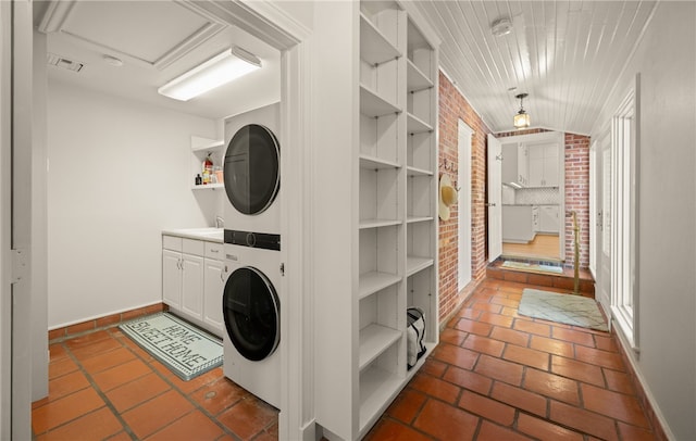 laundry area with stacked washing maching and dryer, brick wall, cabinets, and sink