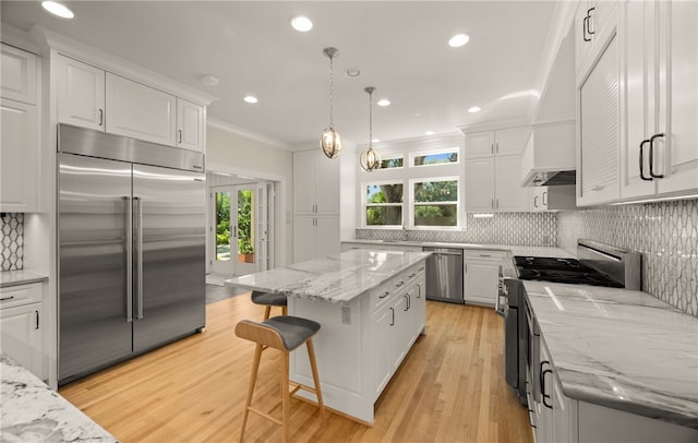 kitchen with light stone counters, white cabinets, a kitchen island, appliances with stainless steel finishes, and decorative light fixtures