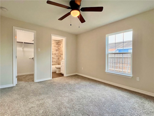 unfurnished bedroom featuring ensuite bathroom, carpet, ceiling fan, a closet, and a walk in closet