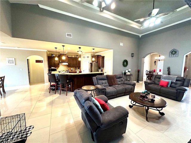 living room with a towering ceiling, light tile patterned floors, ceiling fan, a tray ceiling, and crown molding