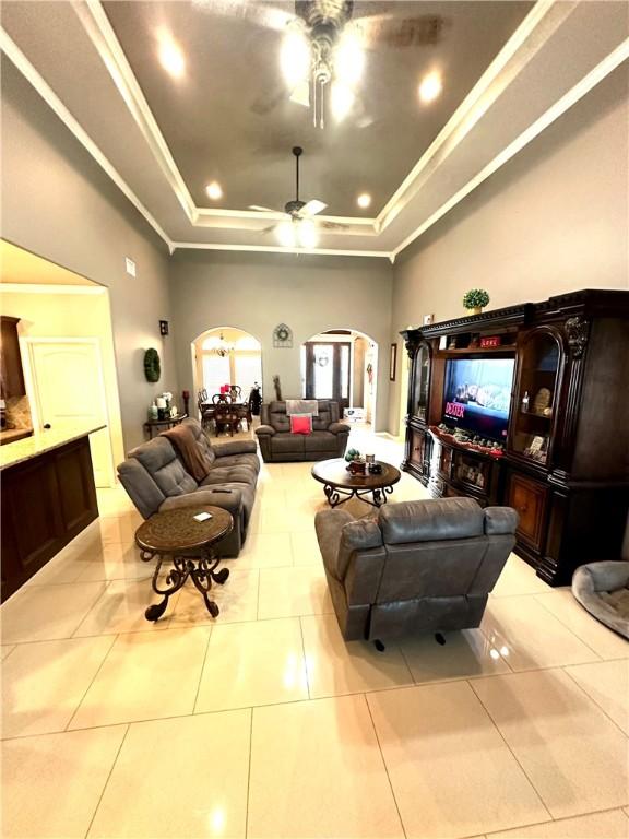 tiled living room featuring ceiling fan, ornamental molding, and a tray ceiling