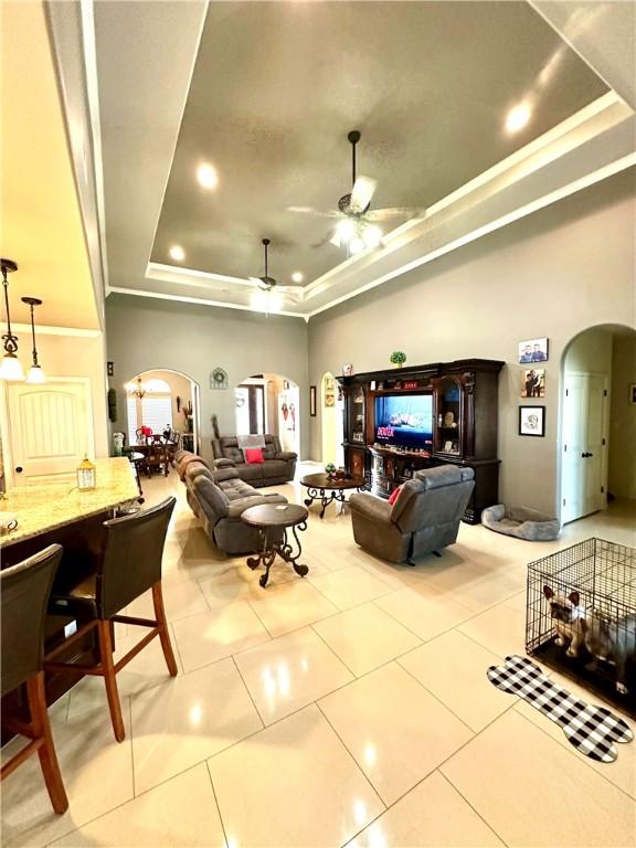 living room with light tile patterned flooring, ceiling fan, and a raised ceiling