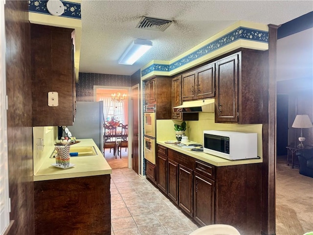 kitchen with dark brown cabinetry, white appliances, wallpapered walls, visible vents, and under cabinet range hood