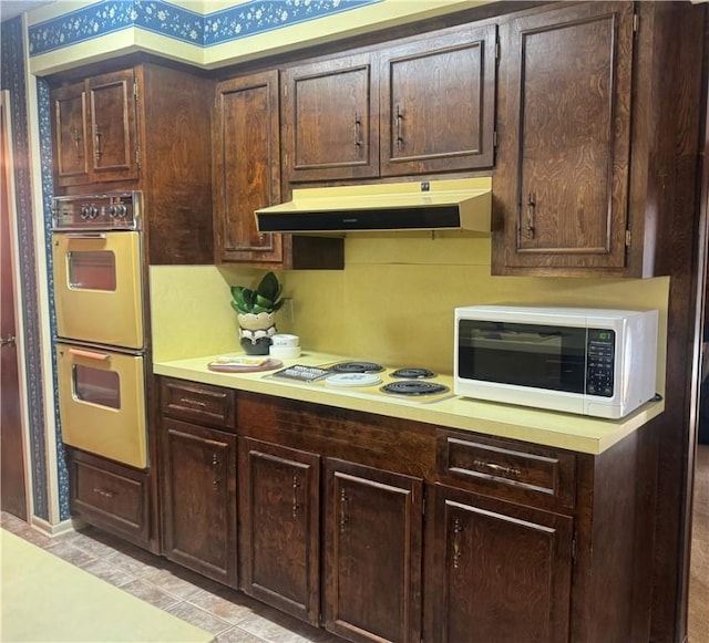 kitchen featuring light countertops, white appliances, dark brown cabinetry, and under cabinet range hood