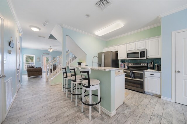 kitchen featuring light hardwood / wood-style floors, white cabinetry, light stone counters, appliances with stainless steel finishes, and a breakfast bar area