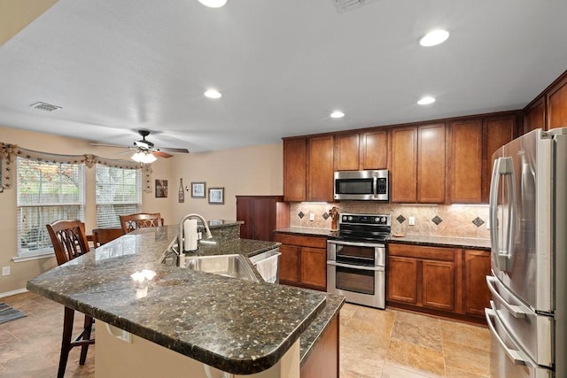 kitchen with appliances with stainless steel finishes, sink, a breakfast bar area, backsplash, and a large island with sink