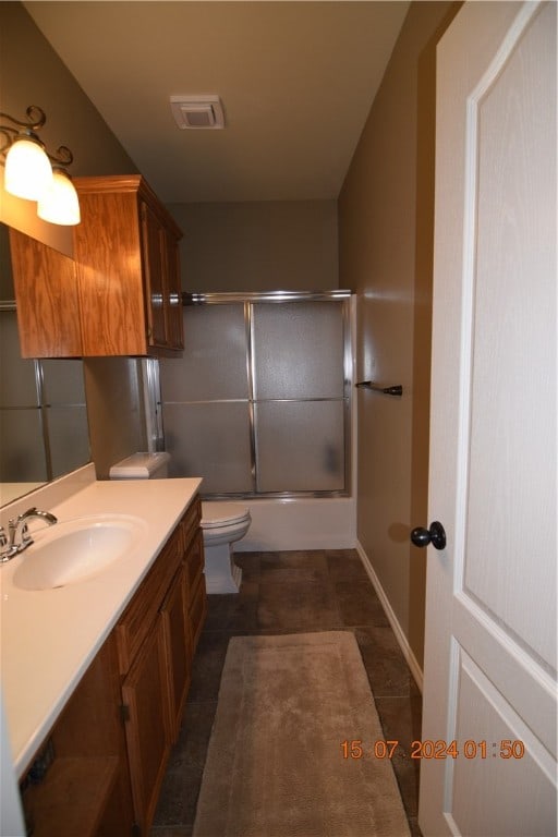 full bathroom with bath / shower combo with glass door, vanity, tile patterned floors, and toilet