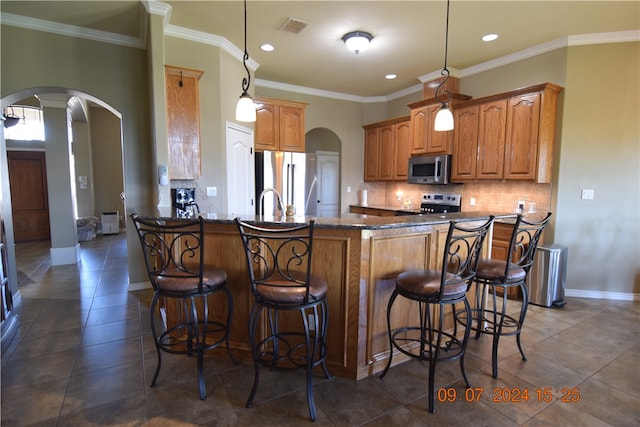 kitchen featuring kitchen peninsula, appliances with stainless steel finishes, a kitchen breakfast bar, ornamental molding, and pendant lighting