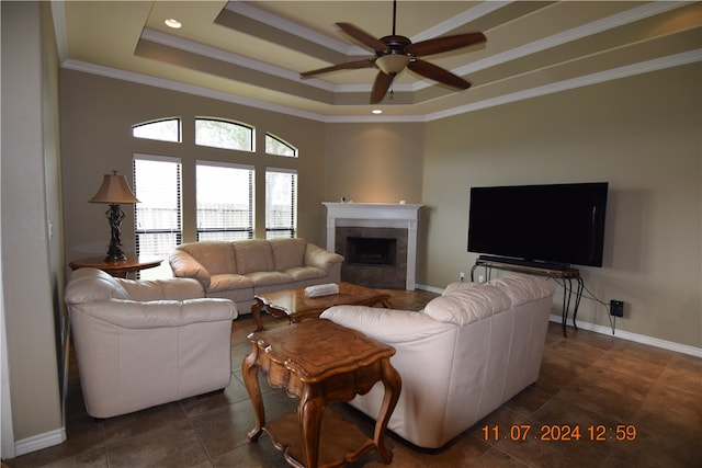 tiled living room with ornamental molding, a tiled fireplace, ceiling fan, and a raised ceiling