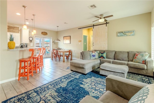 living room with ceiling fan, a barn door, and visible vents