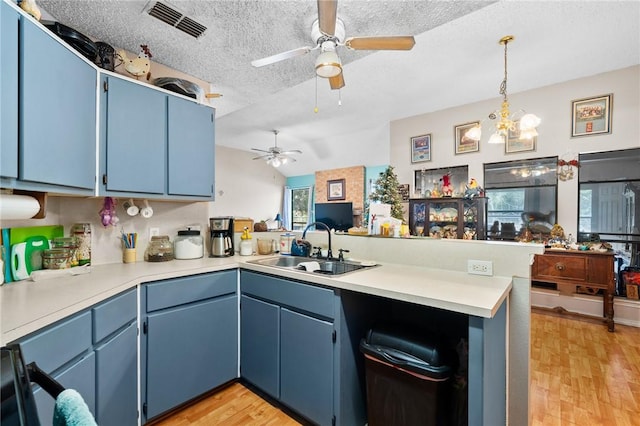 kitchen featuring blue cabinets, sink, hanging light fixtures, light wood-type flooring, and kitchen peninsula