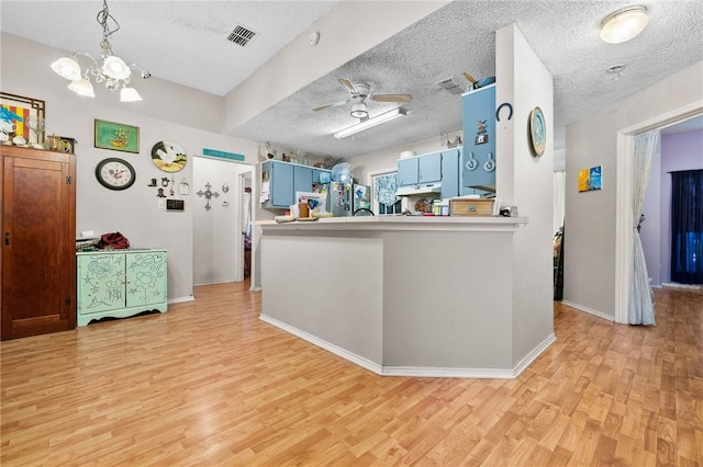 kitchen with blue cabinetry, light hardwood / wood-style flooring, stainless steel refrigerator, kitchen peninsula, and ceiling fan with notable chandelier