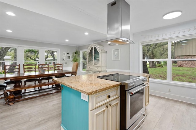 kitchen featuring light wood-type flooring, light stone counters, high end stove, island range hood, and a center island