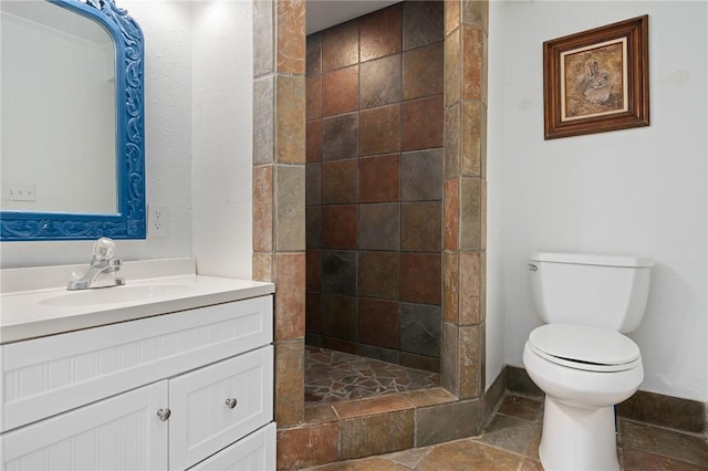 bathroom featuring a tile shower, vanity, and toilet