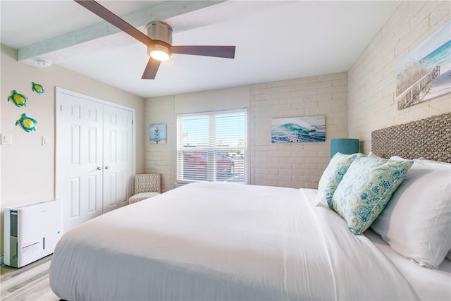 bedroom with ceiling fan, brick wall, a closet, beamed ceiling, and light wood-type flooring