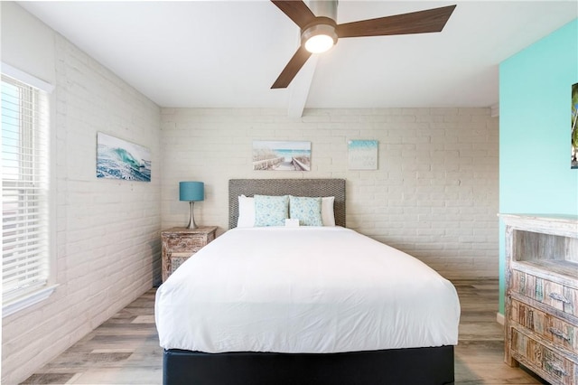 bedroom featuring beamed ceiling, ceiling fan, brick wall, and light hardwood / wood-style flooring