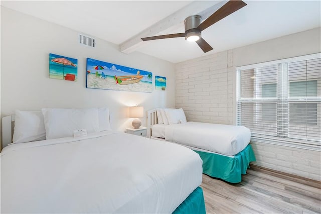 bedroom featuring beam ceiling, brick wall, ceiling fan, and light wood-type flooring