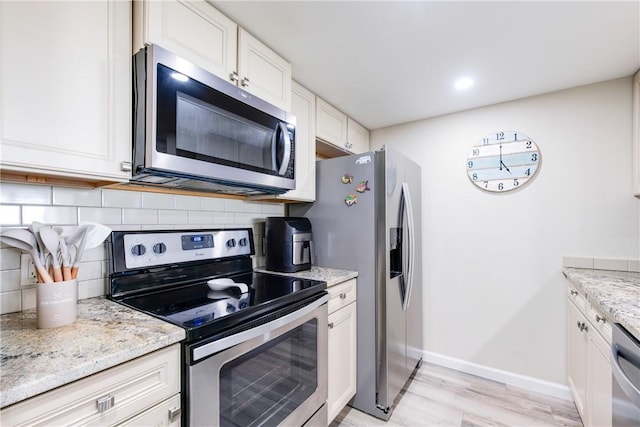 kitchen featuring stainless steel appliances, light stone countertops, decorative backsplash, and white cabinets