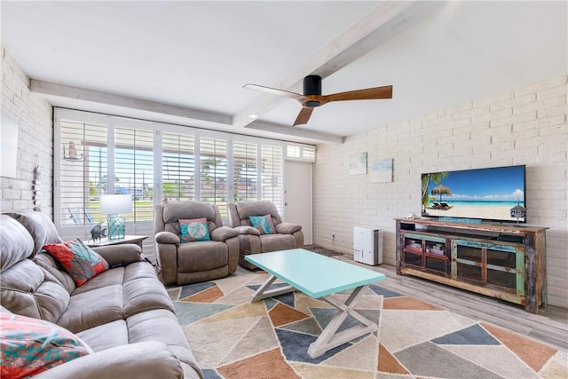 living room featuring ceiling fan, brick wall, light wood-type flooring, and beam ceiling