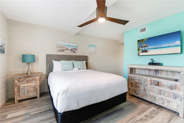 bedroom with beamed ceiling, brick wall, hardwood / wood-style floors, and ceiling fan