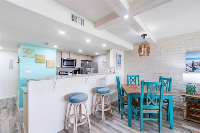 kitchen with pendant lighting, light hardwood / wood-style flooring, stainless steel appliances, and beamed ceiling