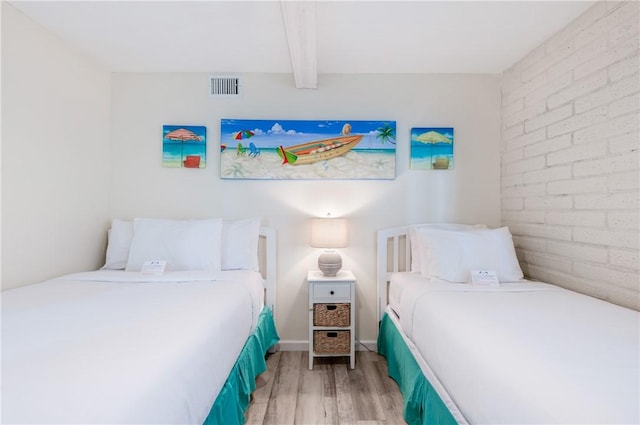 bedroom featuring beam ceiling, brick wall, and light wood-type flooring