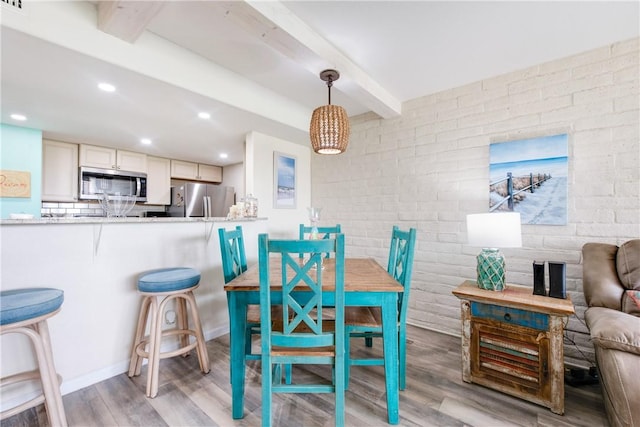 dining room featuring hardwood / wood-style flooring, beamed ceiling, and brick wall