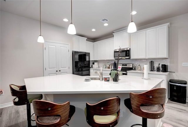 kitchen with stainless steel appliances, a kitchen island with sink, hanging light fixtures, and white cabinets