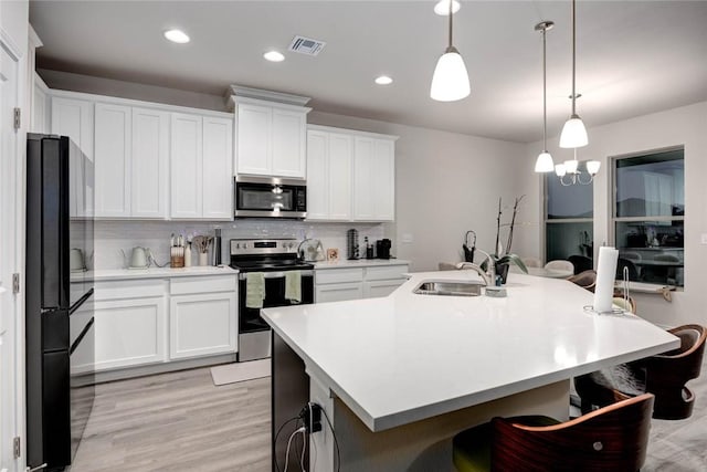 kitchen with pendant lighting, white cabinetry, stainless steel appliances, and a center island with sink