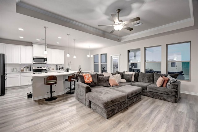 living room featuring crown molding, a tray ceiling, ceiling fan with notable chandelier, and light hardwood / wood-style floors