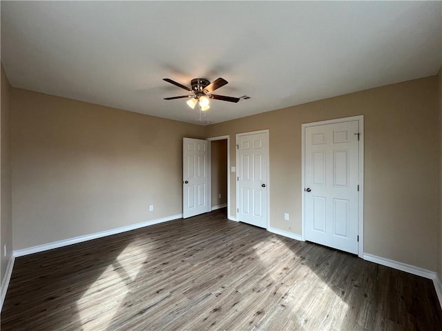 unfurnished bedroom featuring hardwood / wood-style floors, ceiling fan, and multiple closets