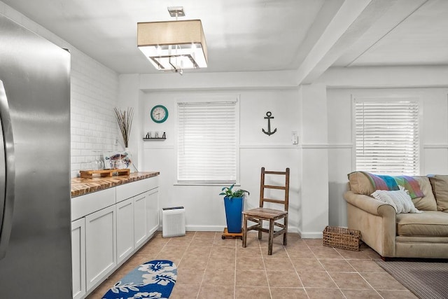 kitchen featuring light tile patterned floors, white cabinetry, baseboards, decorative backsplash, and stainless steel fridge