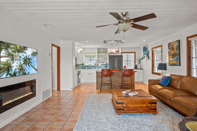 living room with light tile patterned floors, ceiling fan, and a glass covered fireplace