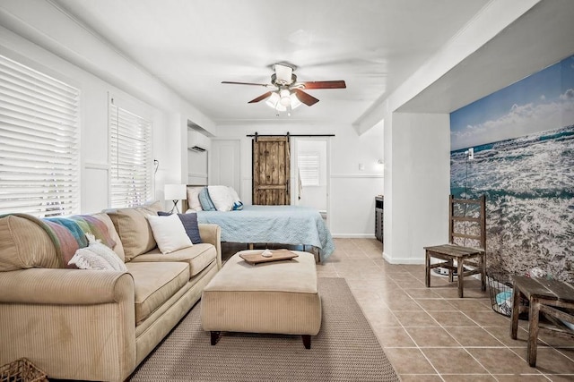 bedroom featuring light tile patterned floors, a barn door, baseboards, a ceiling fan, and a wall mounted air conditioner