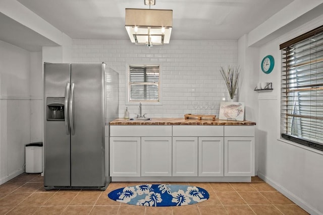 kitchen featuring light tile patterned floors, a sink, white cabinets, stainless steel fridge with ice dispenser, and decorative backsplash