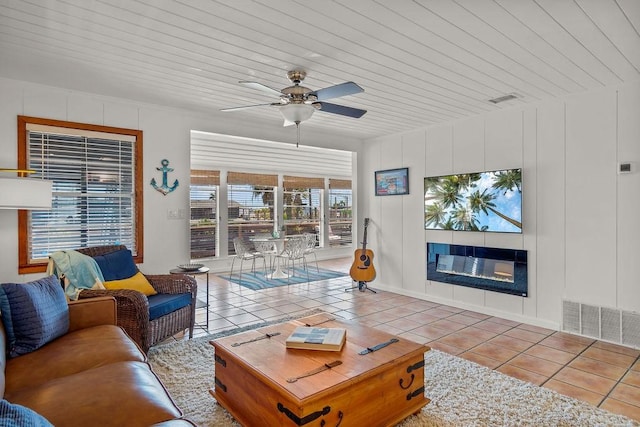 living area with visible vents, a glass covered fireplace, ceiling fan, a decorative wall, and light tile patterned flooring