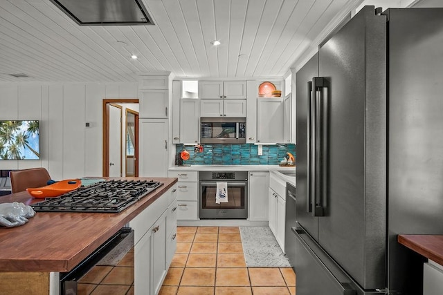 kitchen with stainless steel appliances, backsplash, white cabinets, light tile patterned flooring, and wooden ceiling