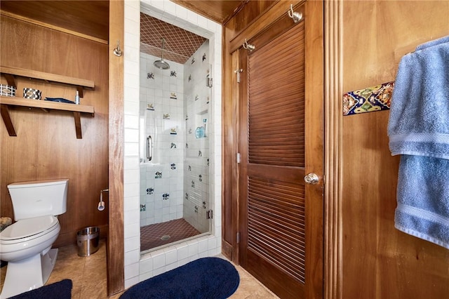 bathroom featuring tile patterned flooring, toilet, a shower with shower door, and wooden walls