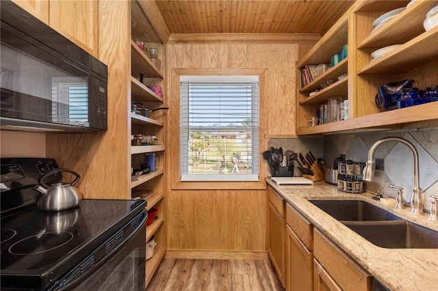 kitchen featuring sink, light stone counters, light hardwood / wood-style floors, wooden walls, and black appliances