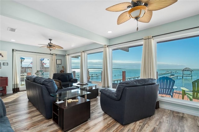 living room featuring ceiling fan, a water view, light wood-type flooring, and french doors