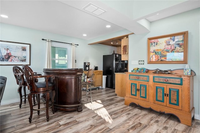 bar with hardwood / wood-style floors and black fridge