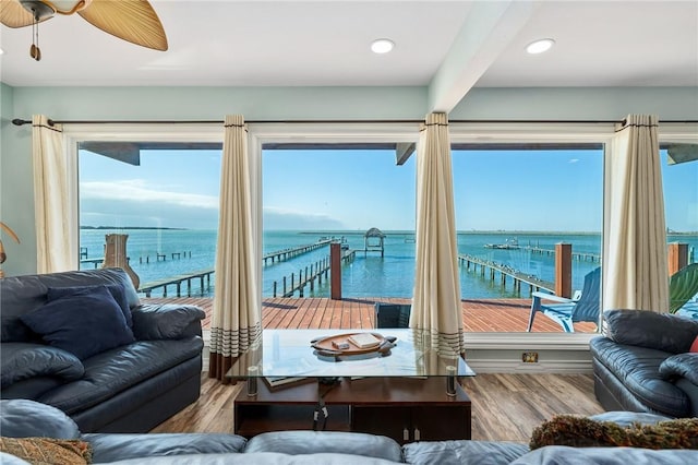 living room with light wood-type flooring, a water view, ceiling fan, and a healthy amount of sunlight