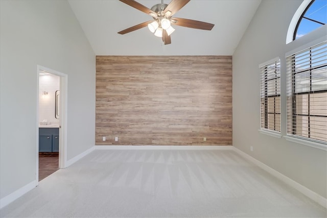 carpeted empty room with high vaulted ceiling, wooden walls, and ceiling fan