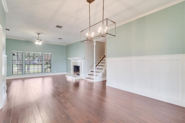 unfurnished living room featuring ceiling fan with notable chandelier, dark wood-type flooring, and crown molding