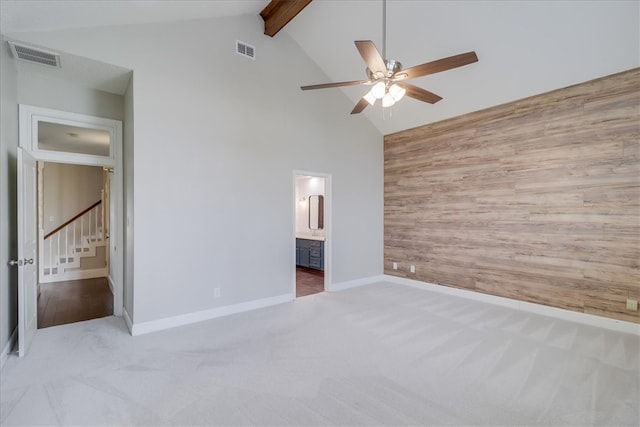 unfurnished bedroom featuring ensuite bath, beam ceiling, wooden walls, light colored carpet, and ceiling fan