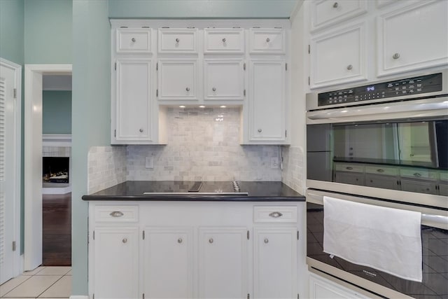 kitchen featuring cooktop, light tile patterned floors, tasteful backsplash, stainless steel double oven, and white cabinetry