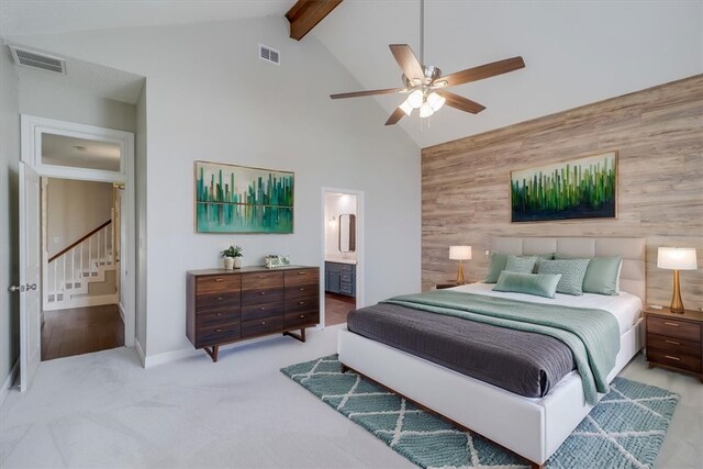 carpeted bedroom featuring wood walls, ensuite bathroom, high vaulted ceiling, beamed ceiling, and ceiling fan