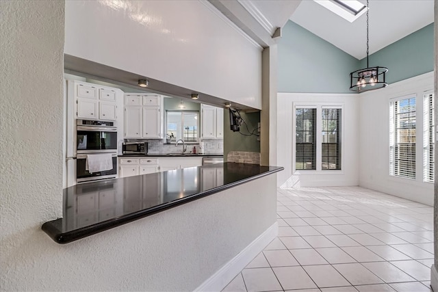 kitchen with stainless steel appliances, light tile patterned flooring, high vaulted ceiling, a skylight, and white cabinets