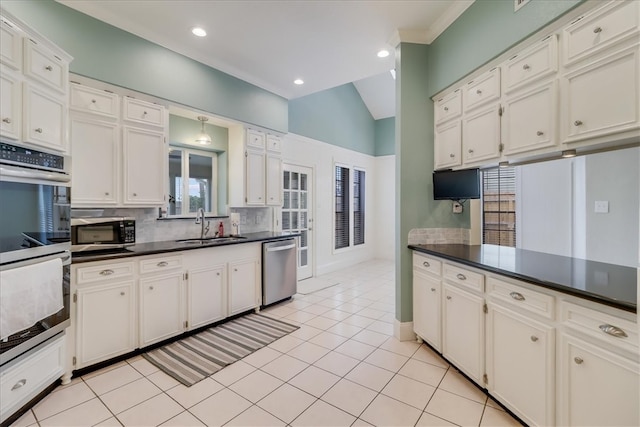 kitchen with appliances with stainless steel finishes, light tile patterned floors, sink, vaulted ceiling, and white cabinets