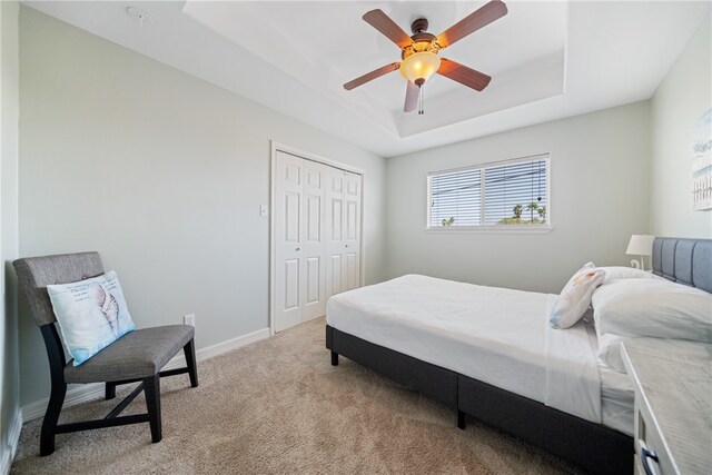 carpeted bedroom with ceiling fan, a closet, and a tray ceiling